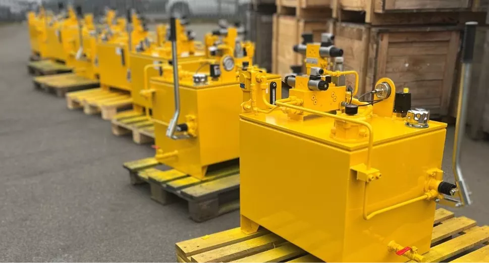 A row of 4 hydraulic power units, all identical, cream coloured, ready for shipping